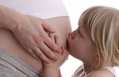 little girl kissing pregnant belly of her mum
