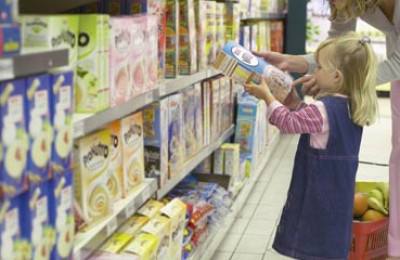 Portrait of a small girl holding a box of cereal as she shops with her mother in a grocery store